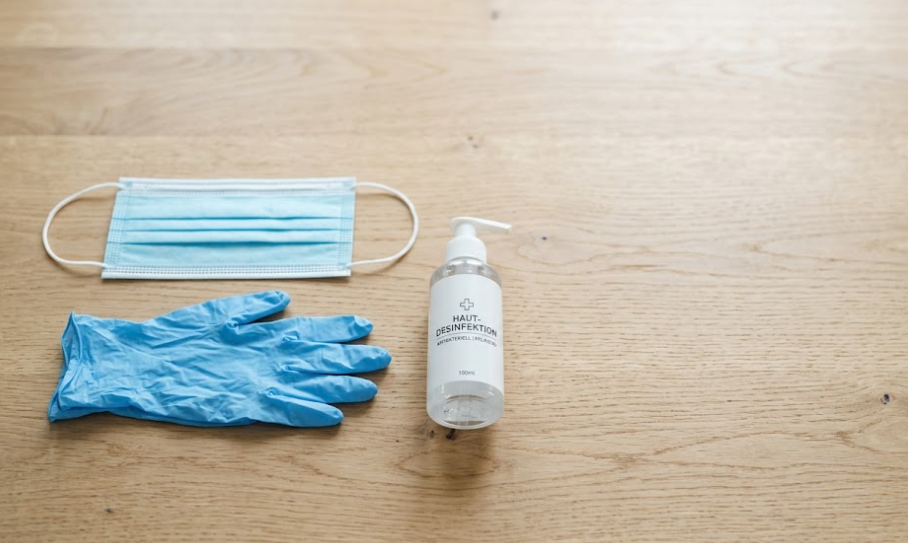 Mundschutz, Einmalhandschuhe und Händedesinfektion auf einem Holztisch.